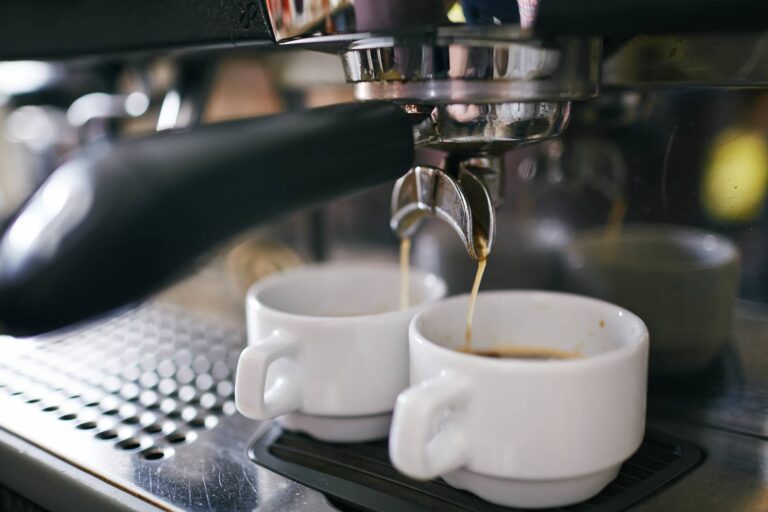 Black coffee pouring in two porcelain cups in coffee machine