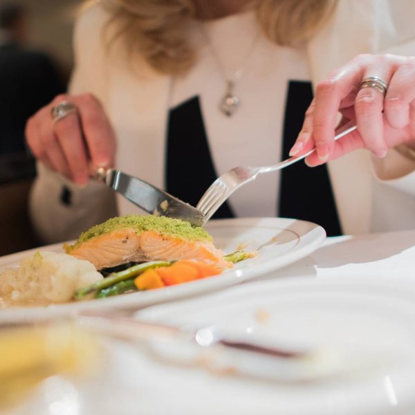 Elegant Restaurant Dinner. Grilled Salmon with Vegetables. Woman Eating Dinner.