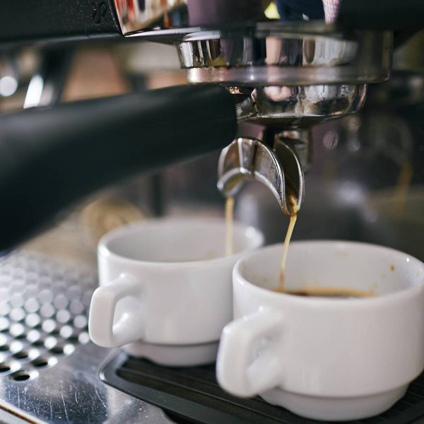 Black coffee pouring in two porcelain cups in coffee machine